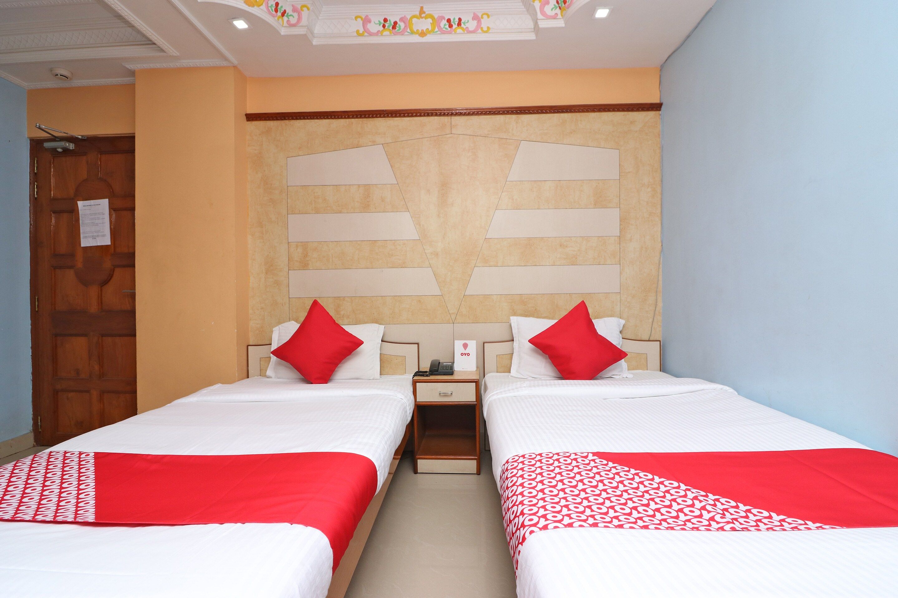 Habitación de hotel con dos camas, una puerta de madera y una pared con un diseño decorativo.