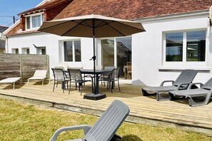 Une terrasse avec une table et des chaises, un grand parasol et des fauteuils de jardin.