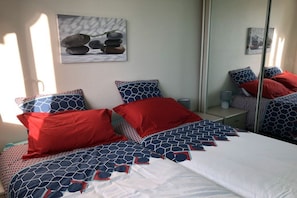Ein Schlafzimmer mit einem Bett, Kissen, einem Nachttisch, einem Spiegel und Wandbildern.
