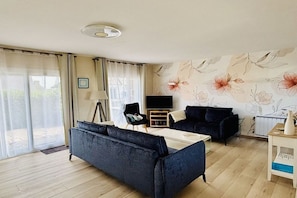 Ein modernes Wohnzimmer mit einem dunkelblauen Sofa, einem weißen Couchtisch, einem schwarzen Sessel und einem Fernseher auf einem Schrank.