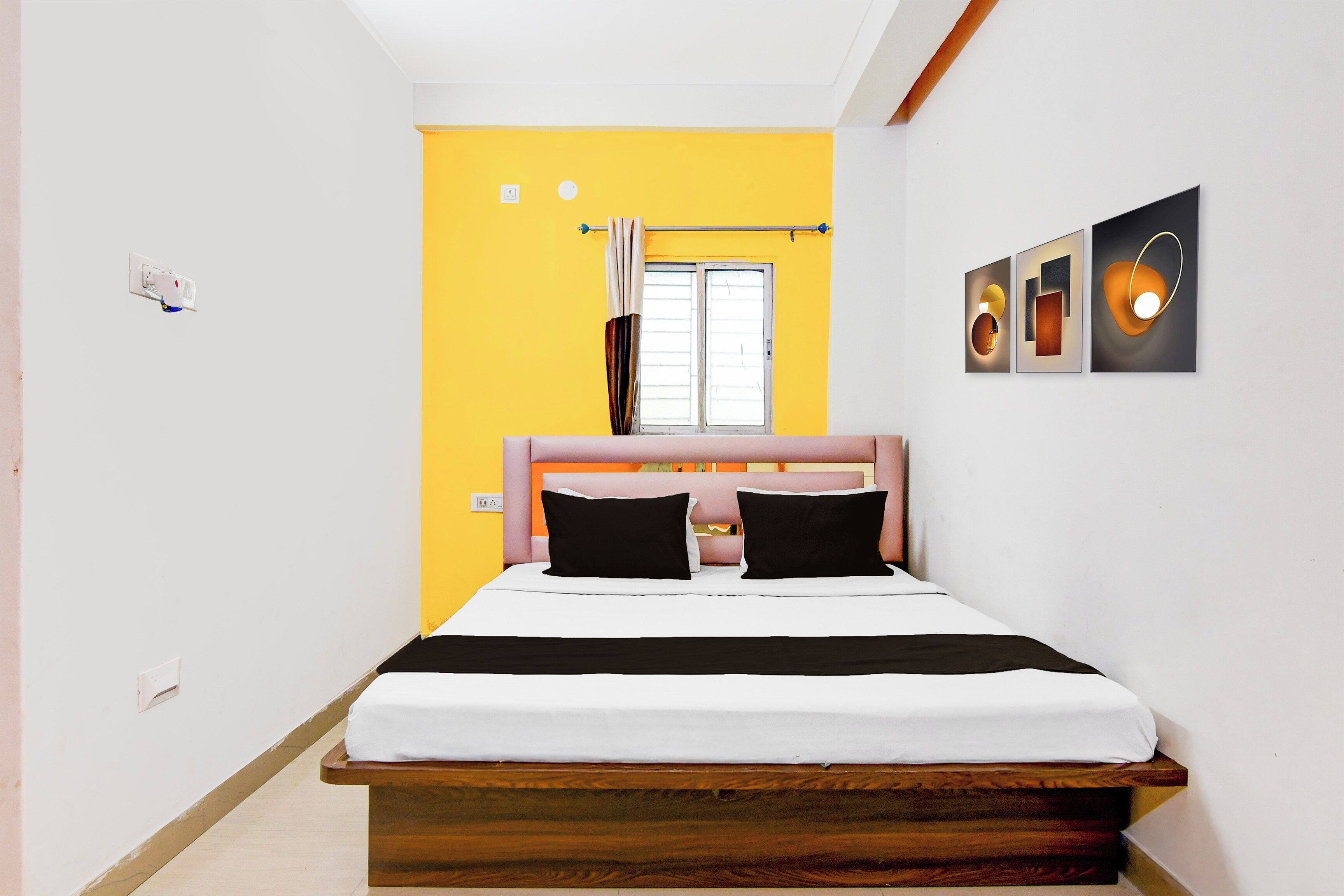 A bedroom with a bed, a window with curtains, and wall-mounted artwork.