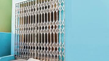 Una verja de metal con diseño de rombos, adosada a un edificio de fachada azul y verde.