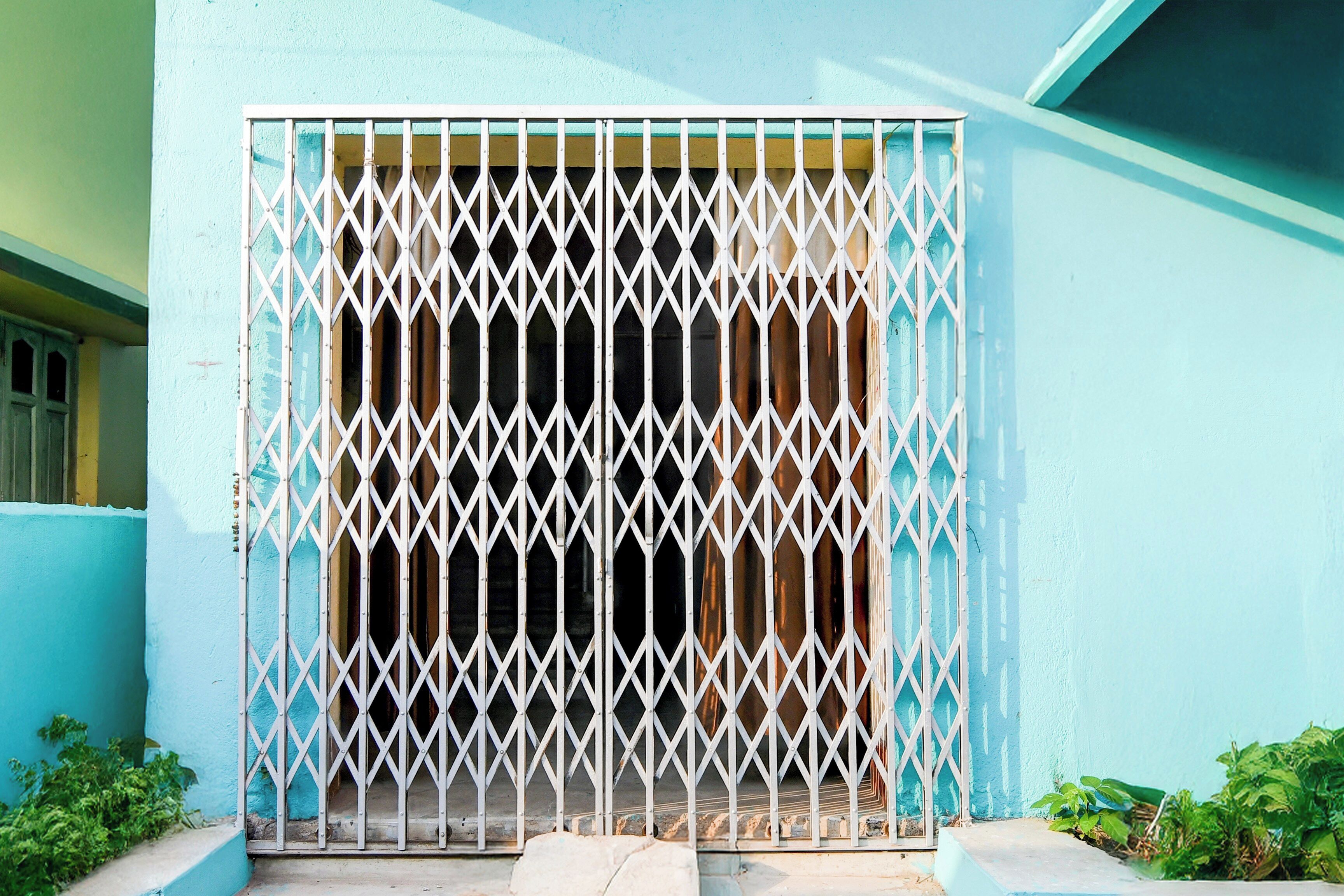 Fachada de edificio con exterior azul y una reja metálica de seguridad.