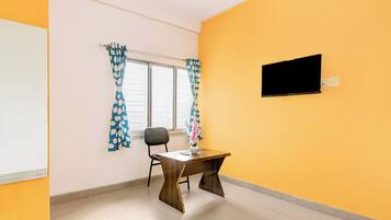 A room with a single table, a chair, a window with curtains, and a mounted television.