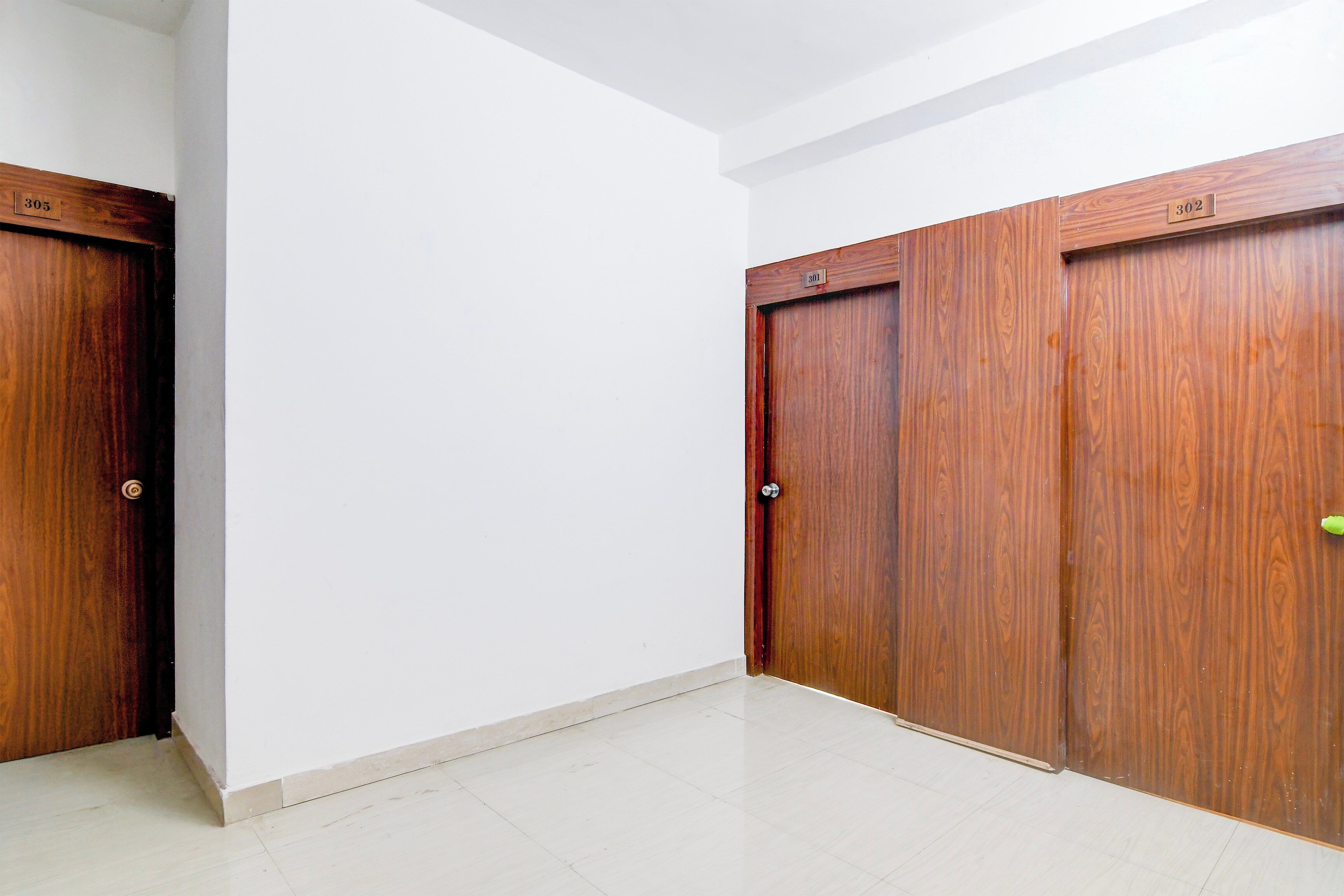 Una habitación con paredes blancas, piso de baldosas y tres puertas de madera con números visibles.