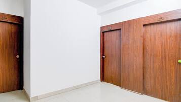 Una habitación con paredes blancas, piso de baldosas y tres puertas de madera con números visibles.