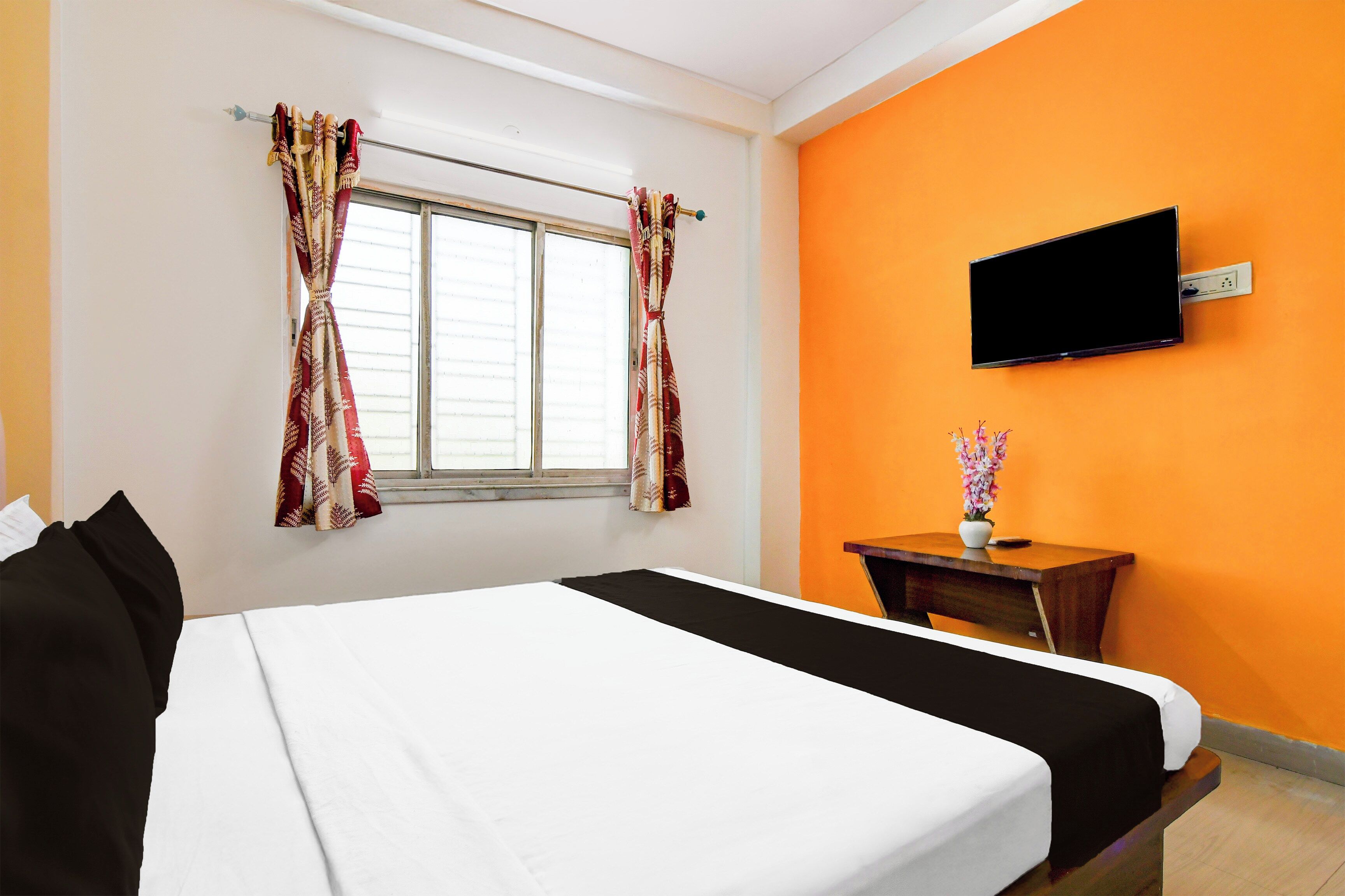 A hotel room with a bed, a television mounted on the wall, and a window with curtains.