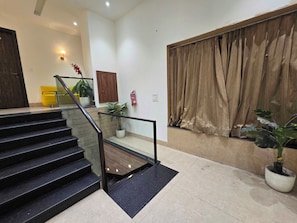 A staircase with a glass railing leading to a landing, a fire extinguisher mounted on the wall, and a large window with curtains. - Hotel O cloud 9 (Amritsar)