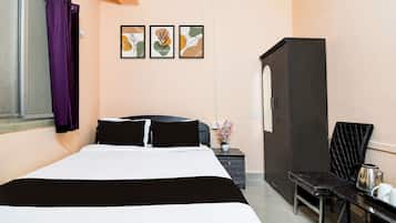 A hotel room with a bed, a wardrobe, a desk with a chair, and a window with curtains.