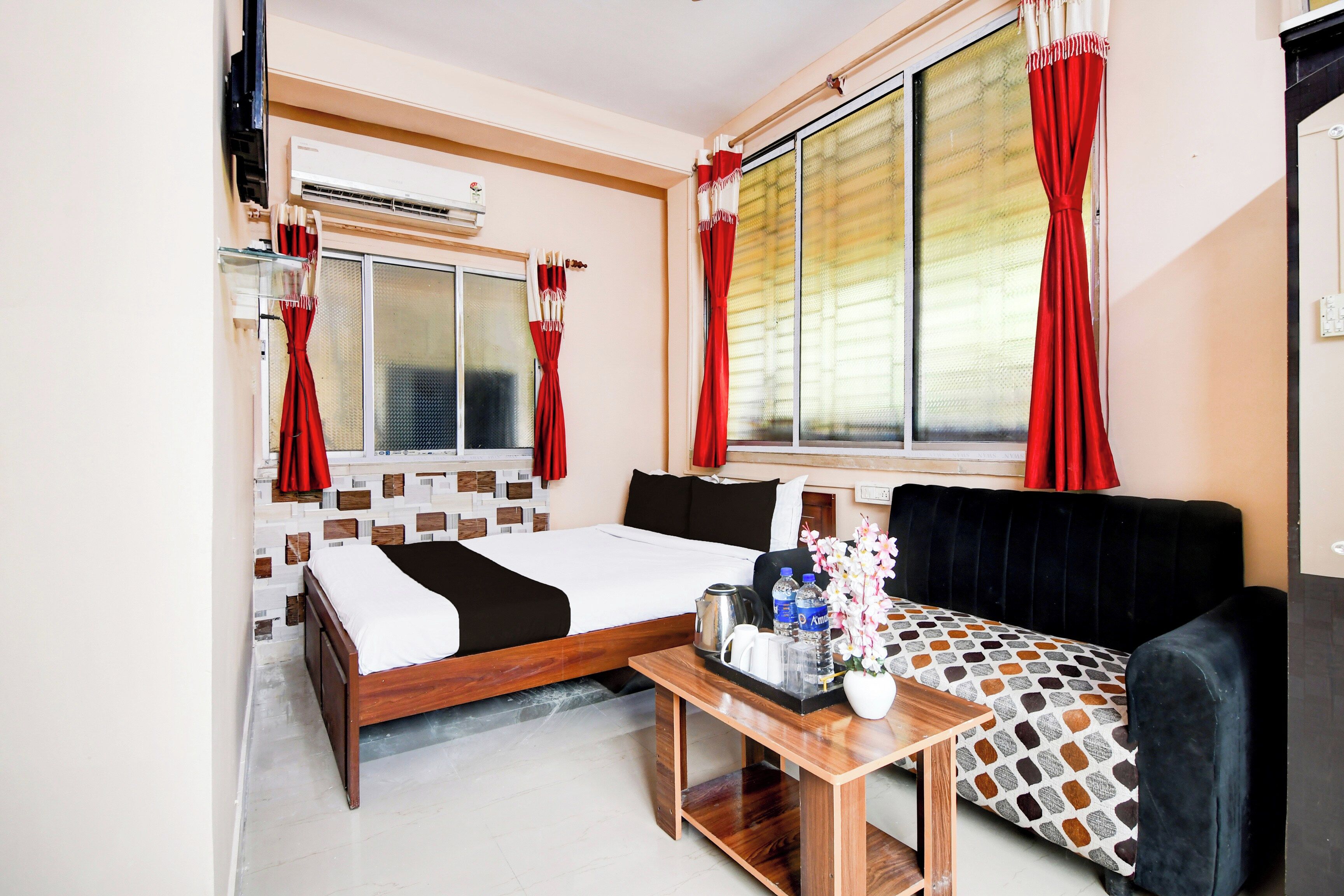 Ein Hotelzimmer mit einem Bett, einem Sofa, einem kleinen Tisch mit Blumen und einem Fenster mit roten Vorhängen.