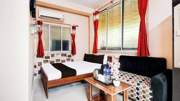 Ein Hotelzimmer mit einem Bett, einem Sofa, einem kleinen Tisch mit Blumen und einem Fenster mit roten Vorhängen.