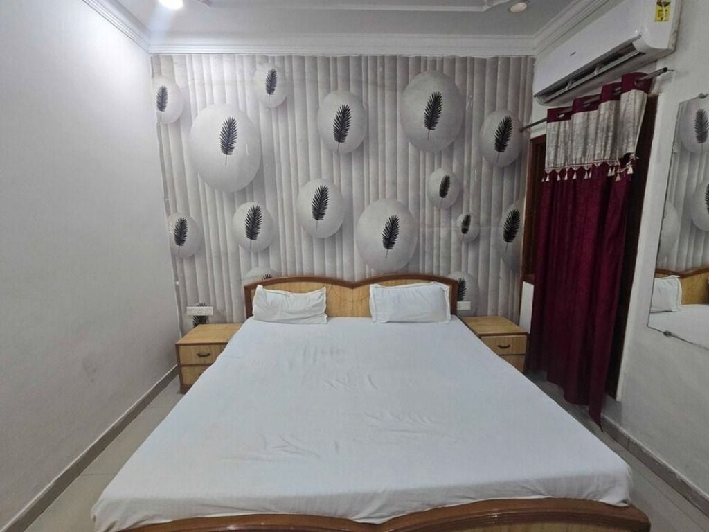 A bedroom with a large bed, two bedside tables, a wall-mounted air conditioner, and a window with curtains.