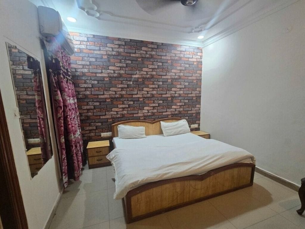 A bedroom with a brick-patterned wall, a wooden bed, a nightstand, and a mirror.