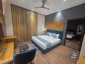 A hotel room with a bed, a desk, a chair, a ceiling fan, and a large window with curtains. - Hotel O Regal (Amritsar)