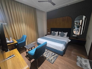 A hotel room with a bed, a desk, a chair, a mirror, and a ceiling fan. - Hotel O Regal (Amritsar)