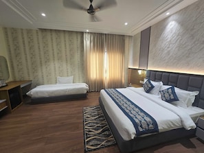A hotel room with two beds, a desk, a mirror, a ceiling fan, and a large wall-mounted light fixture. - Hotel O Regal (Amritsar)