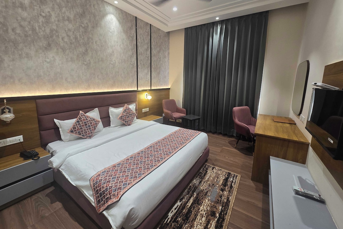 A modern hotel room with a large bed, bedside tables, a desk, a chair, a ceiling fan, and a TV.