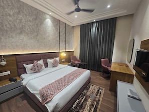 A modern hotel room with a large bed, bedside tables, a desk, a chair, a ceiling fan, and a TV. - Hotel O Regal (Amritsar)