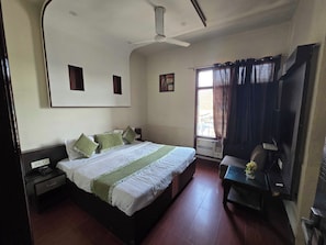 A hotel room with a bed, bedside table, nightstand, window with curtains, and a ceiling fan. - Hotel O Regal (Amritsar)