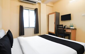 Habitación de hotel con cama, escritorio, silla, televisor y ventana con cortinas.