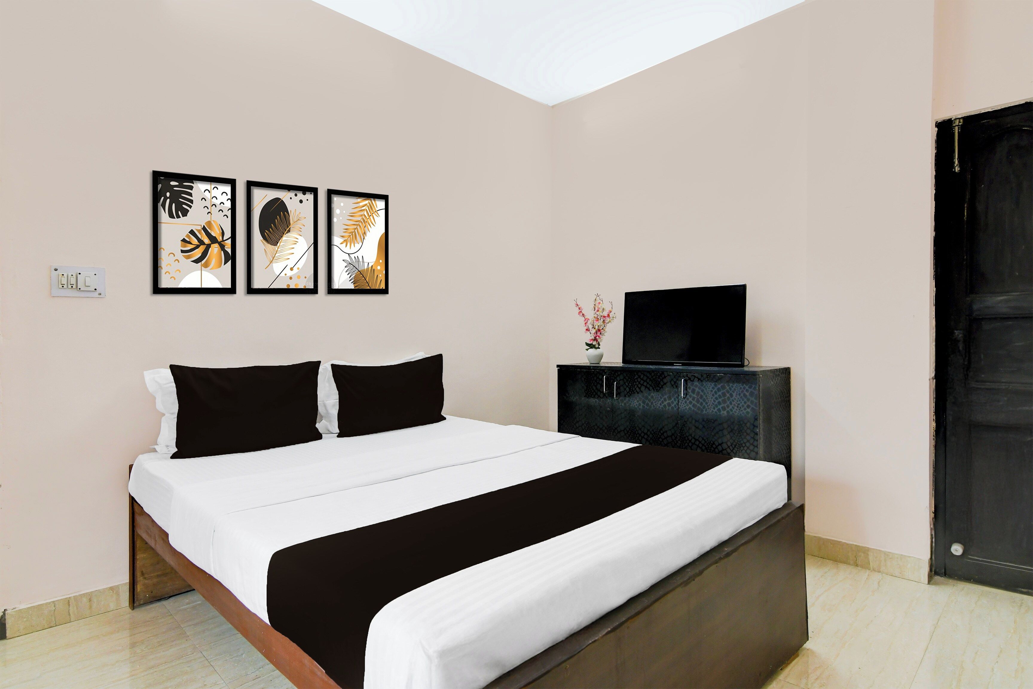 Ein Schlafzimmer mit einem Bett, einem Fernseher auf einer Kommode und drei gerahmten Kunstwerken an der Wand.
