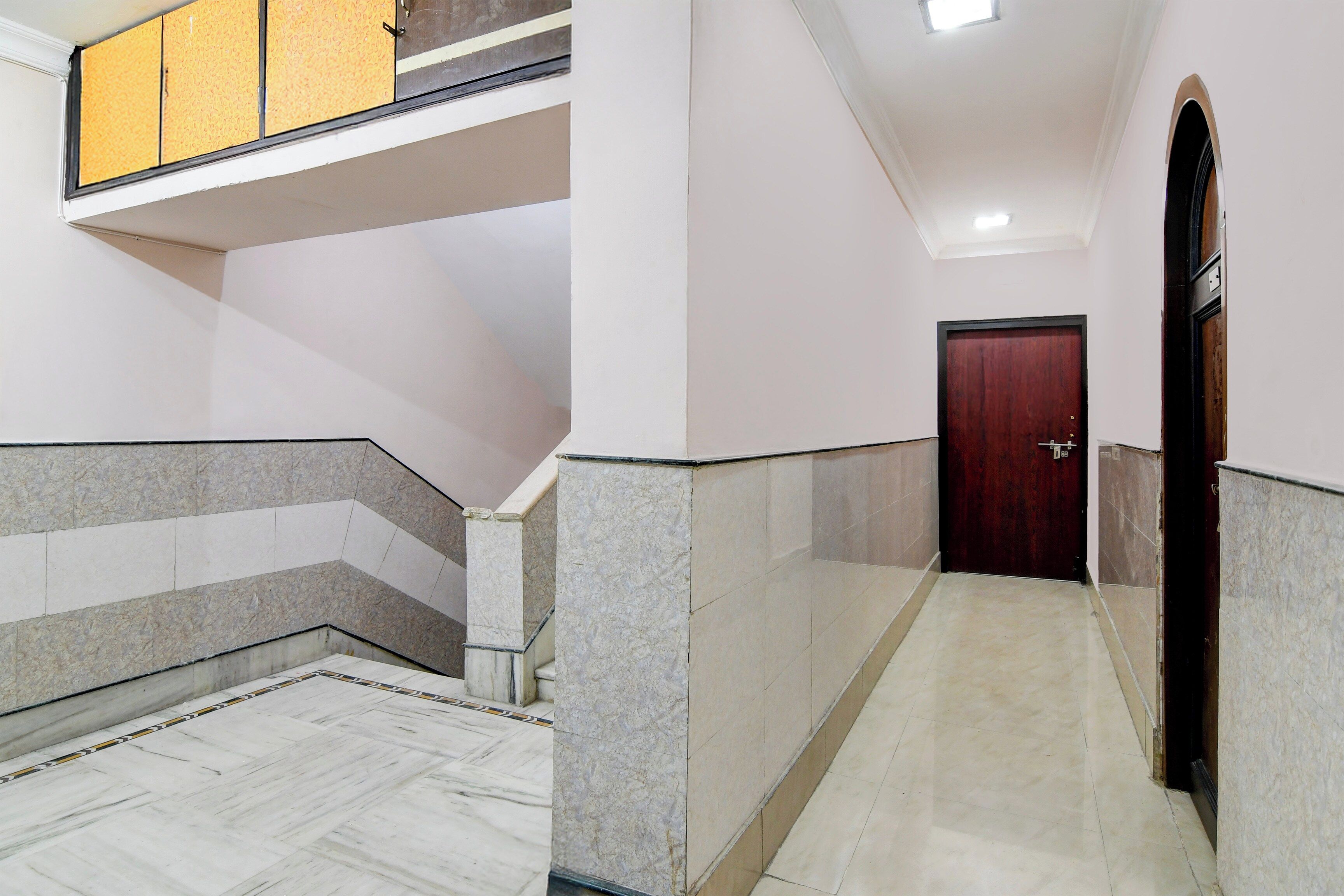 A corridor with marble flooring, a wooden door, and a staircase with a yellow handrail.