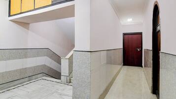 A corridor with marble flooring, a wooden door, and a staircase with a yellow handrail.