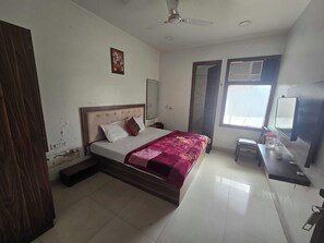 A bedroom with a bed, a ceiling fan, a window, and a desk with a mirror. - Hotel O The fortune grand (Amritsar)