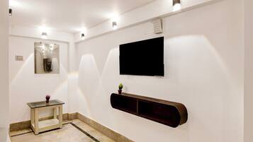 A modern bathroom with a glass table, a mounted TV, and a built-in shelf.