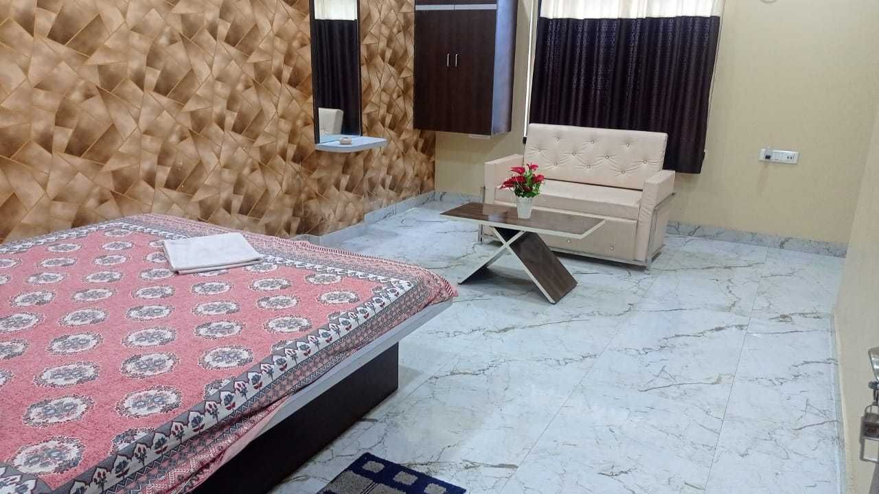 Un dormitorio con cama, sofá, una mesita con un jarrón, espejo y armario.