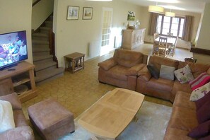 Ein Wohnzimmer mit einer Couch, einem Hocker, einem Couchtisch, einem Fernseher und einer Treppe.