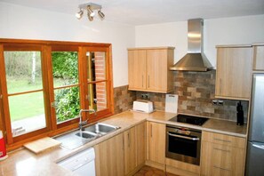 Eine moderne Küche mit Holzausstattung, einem eingebauten Backofen, einer Edelstahl-Dunstabzugshaube und einem Fenster mit Blick auf Grünflächen.