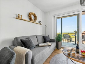Ein modernes Wohnzimmer mit einem grauen Sofa, einem Couchtisch und Blick ins Freie.