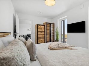 Ein Schlafzimmer mit Bett, Kleiderschrank, Fernseher und einer Pflanze.