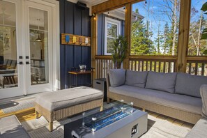 A covered outdoor seating area with a sofa, a glass-top coffee table, and a wicker ottoman. - Riverside Villa - Hot Tub + Games + Fire Pit (Huntsville)