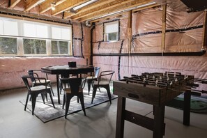 A room with a foosball table, a round table with chairs, and large windows. - Riverside Villa - Hot Tub + Games + Fire Pit (Huntsville)
