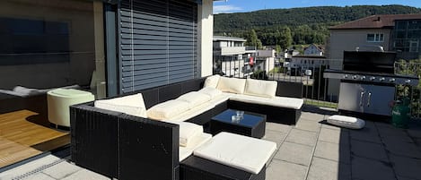 An outdoor patio with a sectional sofa, a small table, and a grill area.