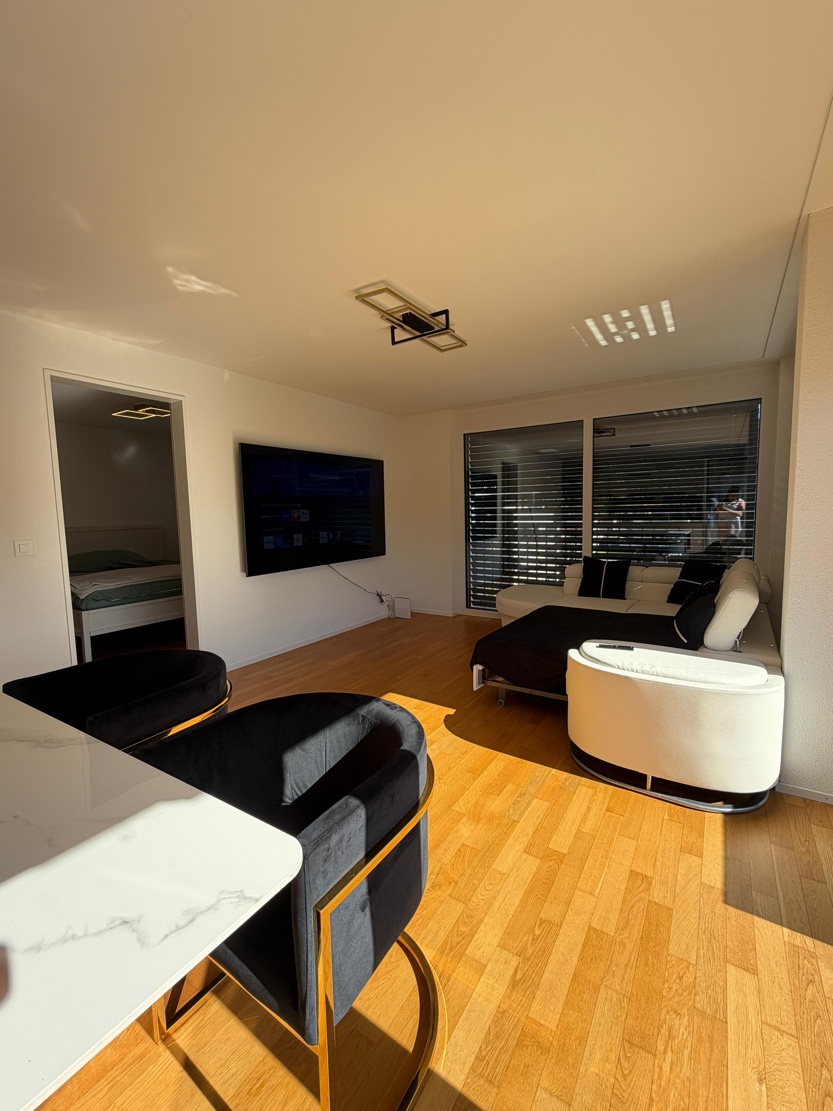 A modern living room with a flat-screen TV mounted on the wall, a sofa, a coffee table, and a dining area with a marble countertop.