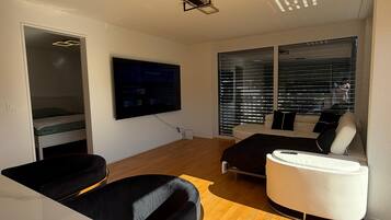A modern living room with a flat-screen TV mounted on the wall, a sofa, a coffee table, and a dining area with a marble countertop.