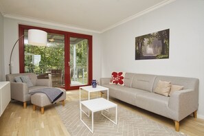 A modern living room with a sofa, a small table, a lamp, and a view through a glass door to an outdoor area. - Modern vacation rental in a quiet location - Haus Fore Vacation Rental No. 202 (Lohme OT Ranzow)