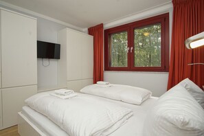 A hotel room with a bed, a TV mounted on the wall, and a window with curtains. - Modern vacation rental in a quiet location - Haus Fore Vacation Rental No. 202 (Lohme OT Ranzow)
