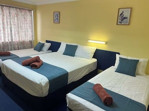 Een hotelkamer met twee bedden, elk met een deken van blauw en wit, en een paar opgerolde handdoeken.