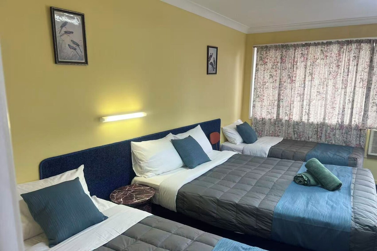 Een hotelkamer met twee bedden, een hoofdbord, een nachtkastje en een raam met gordijnen.