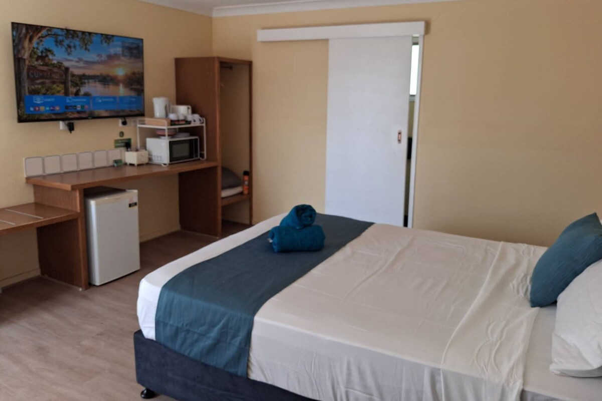 Een hotelkamer met een bed, een bureau met een magnetron, een kleine koelkast en een schilderij aan de muur.