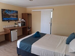 Een hotelkamer met een bed, een bureau met een magnetron, een kleine koelkast en een schilderij aan de muur.