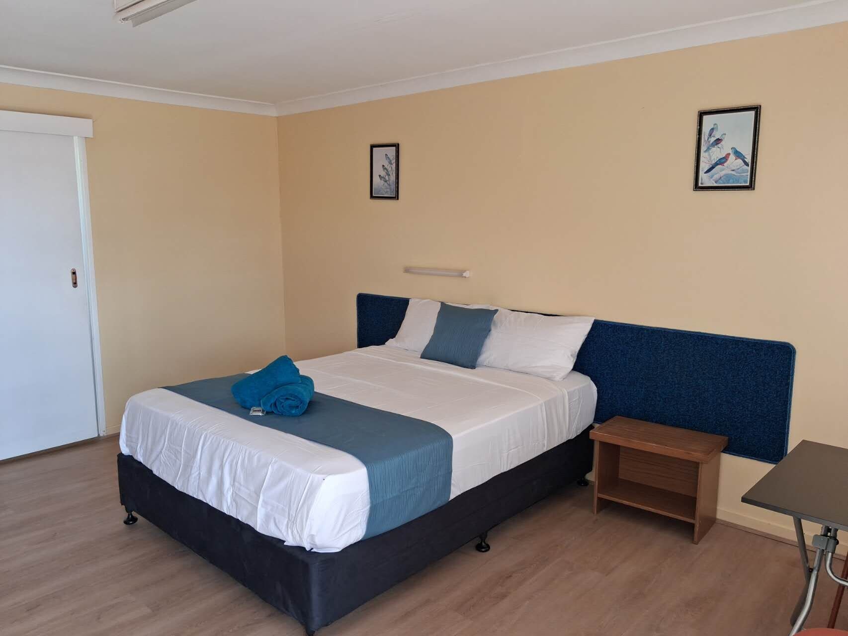 Una habitación de hotel con una cama, una mesita de noche y dos cuadros en la pared.