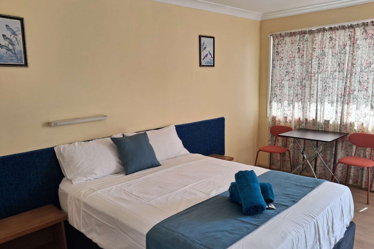 Een hotelkamer met een bed, een kleine tafel met stoelen en een raam met gordijnen.