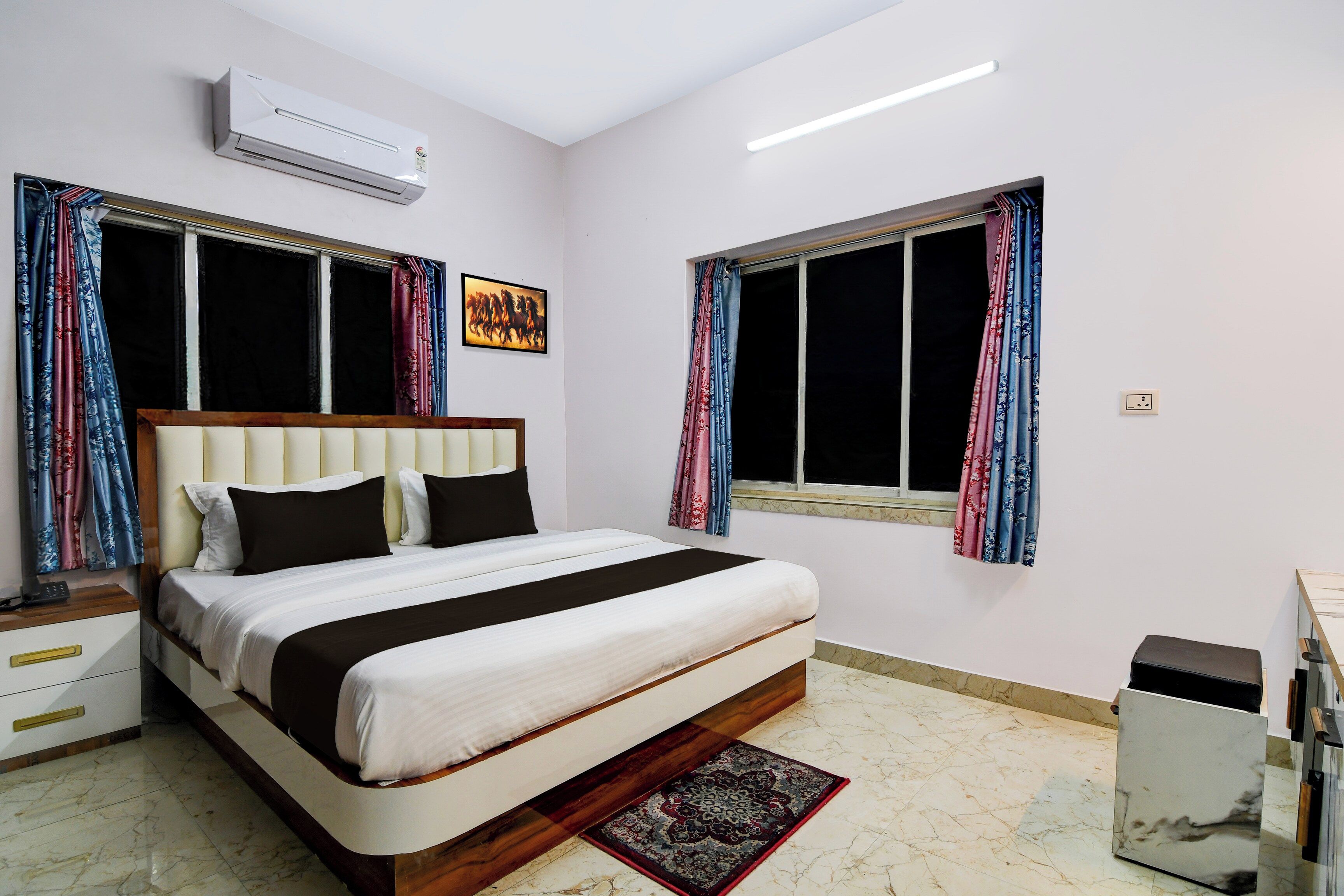 A hotel room with a bed, a desk, an air conditioner, and a window with curtains.