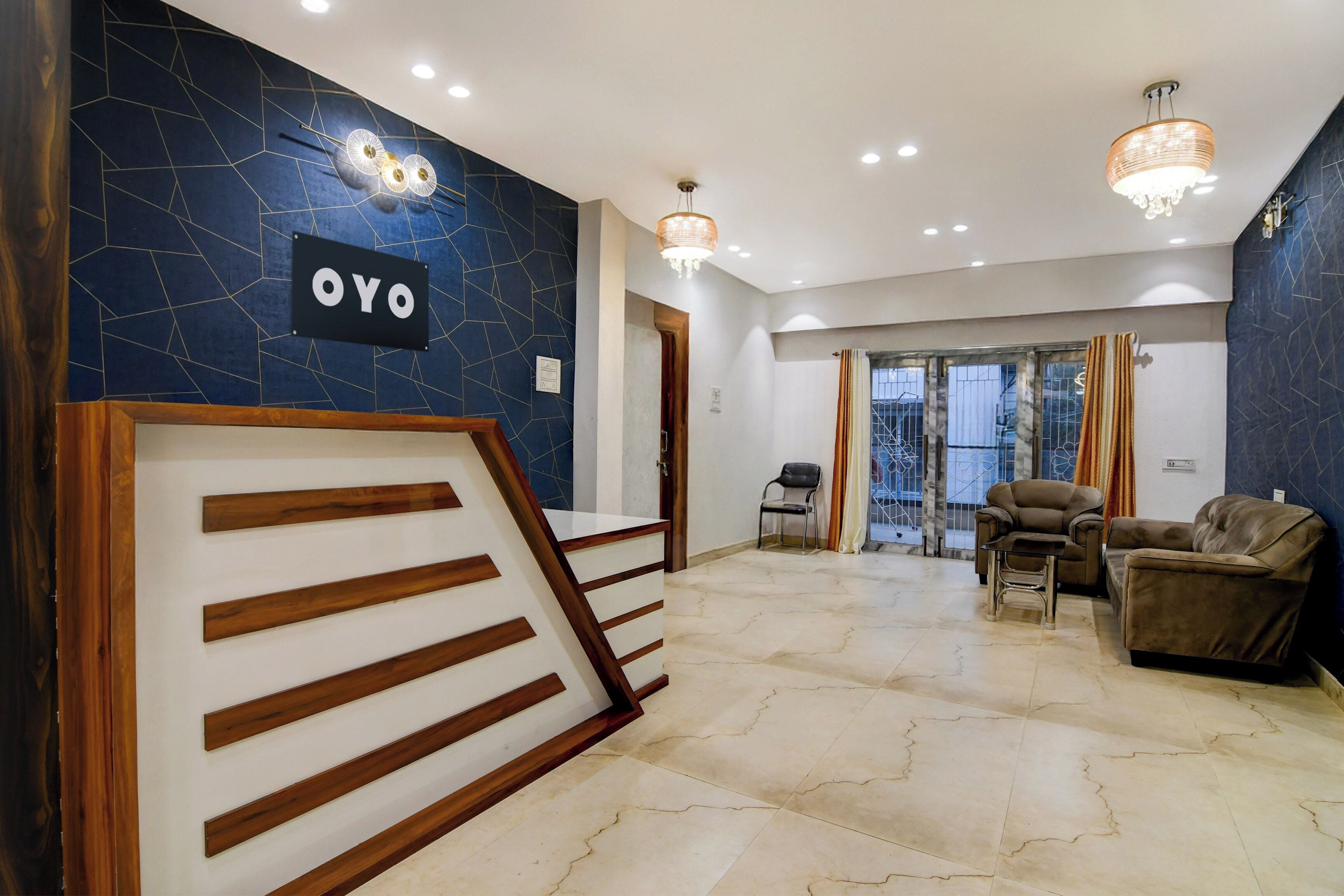 A reception area with a sign reading 'OYO,' a staircase, a seating area with sofas, and a chandelier.