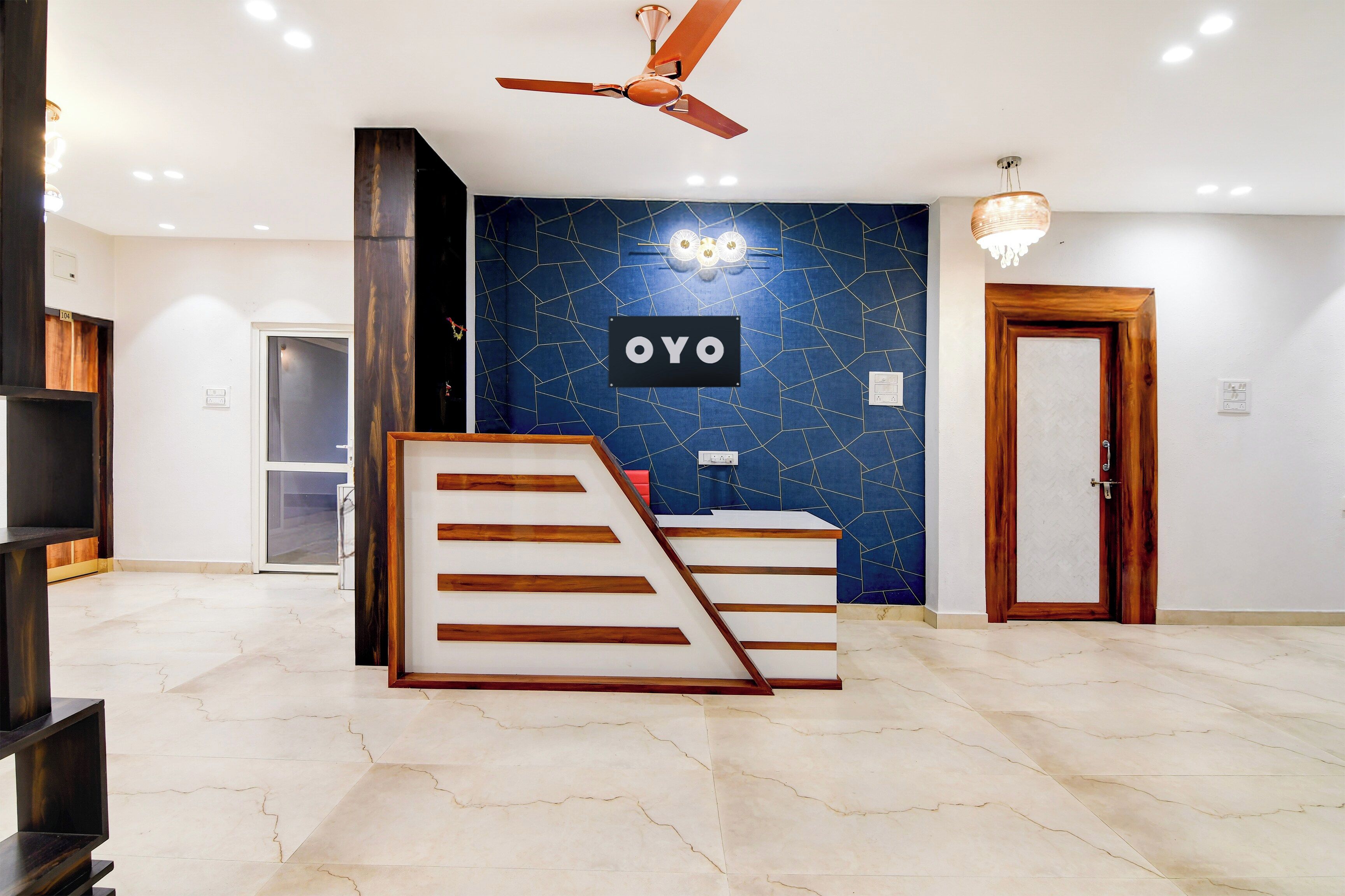A hotel reception area with a modern design, including a reception desk, a ceiling fan, and a wall-mounted sign.